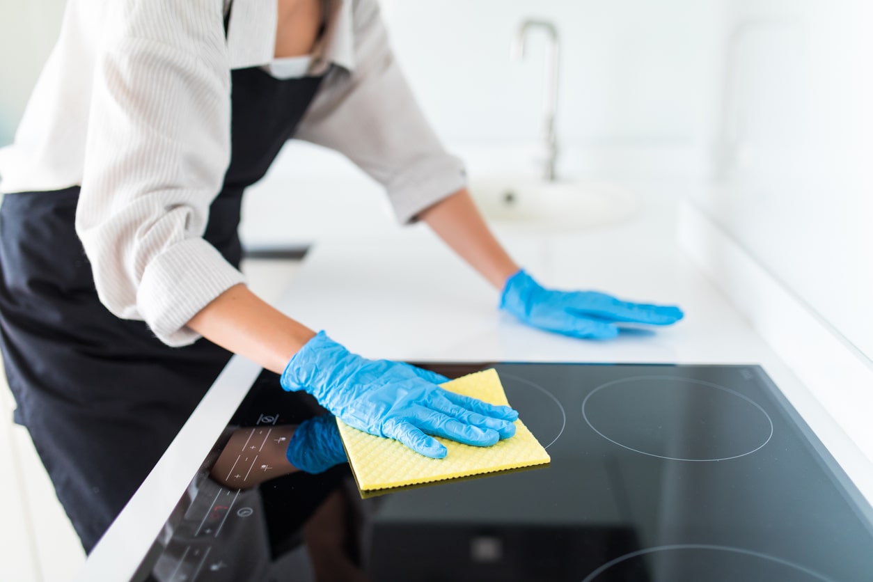 Woman working for a professional cleaning company, wearing gloves while cleaning a residential home's kitchen
